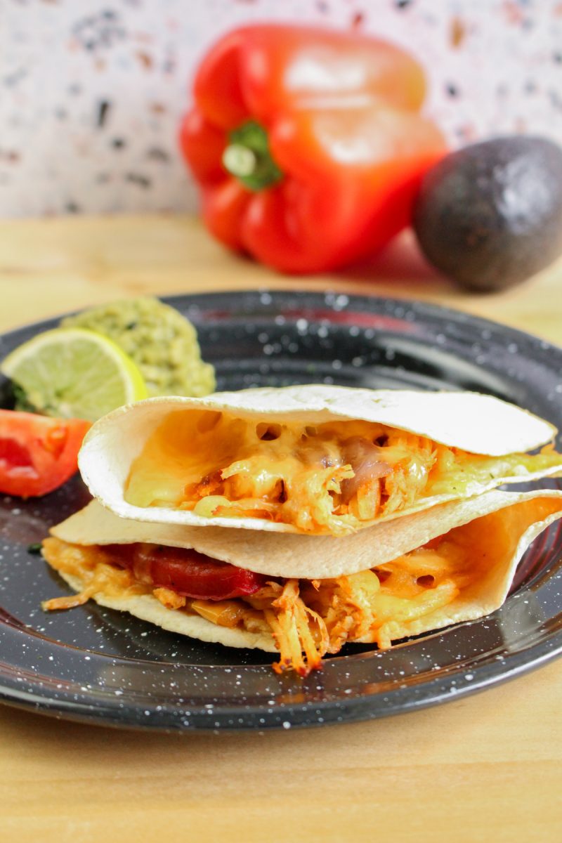 A plate of folded quesadillas with melted cheese and chicken filling, served with guacamole, salsa, and a lime wedge.