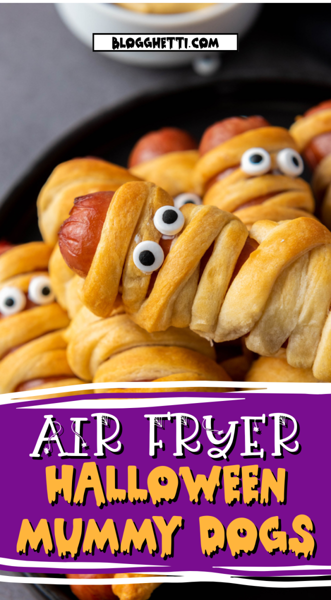 A close-up photo of several air fryer Halloween mummy dogs arranged on a black plate. The mummy dogs are made with hot dogs wrapped in dough and have googly eyes attached.