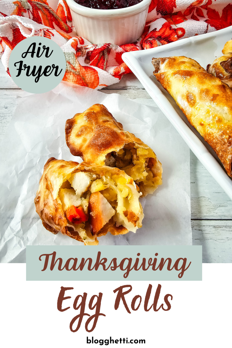 A photo of two air fryer Thanksgiving egg rolls cut in half, revealing a filling of turkey, stuffing, and cranberry sauce. The egg rolls are served on a white plate with parchment paper, and a small bowl of cranberry sauce is visible in the background.