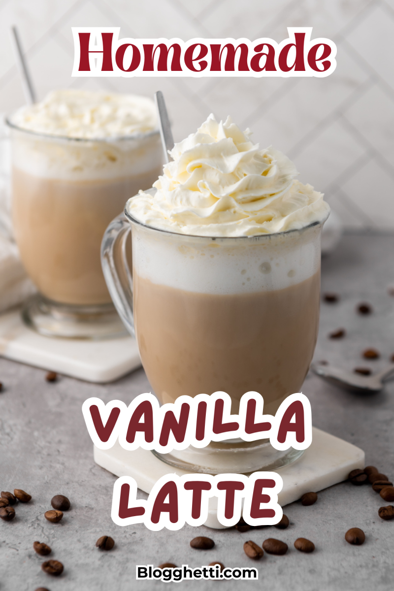 Two glass mugs filled with creamy homemade vanilla lattes topped with swirls of whipped cream. Coffee beans are scattered on the countertop, and a spoon rests nearby. The image includes bold red text overlay reading 'Homemade Vanilla Latte'