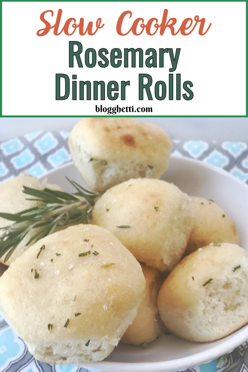 A bowl of soft, golden-brown rosemary dinner rolls made in a slow cooker, garnished with fresh rosemary sprigs. The image features a recipe title at the top in decorative text that reads "Slow Cooker Rosemary Dinner Rolls" The rolls are lightly sprinkled with salt and rosemary, giving them a rustic, homemade look against a patterned background.