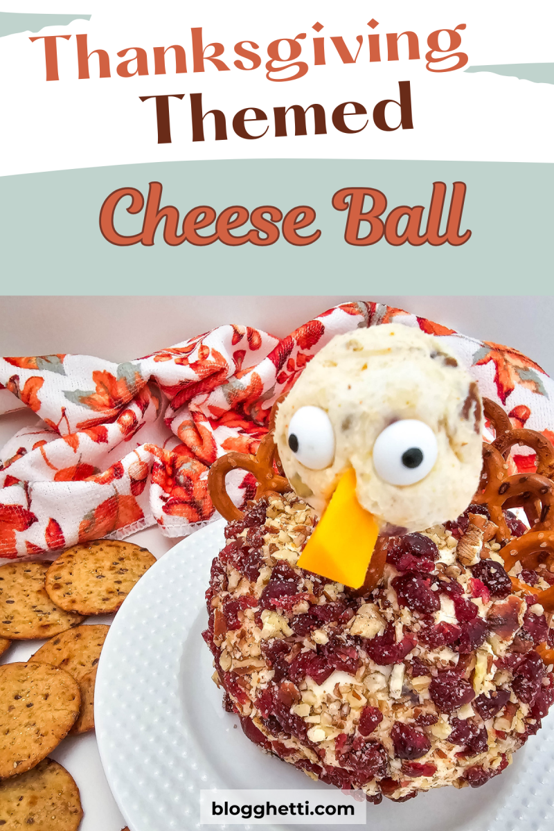 A Thanksgiving-themed cheese ball shaped like a turkey. The cheese ball is decorated with pretzels for legs, candy eyes, a cheese beak, and cranberries. It's served on a white plate with crackers and a festive napkin in the background.