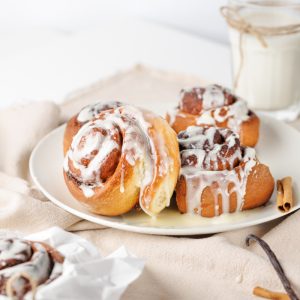 Close-up of warm, gooey homemade cinnamon rolls with a generous drizzle of creamy white cream cheese frosting, served on a white plate.