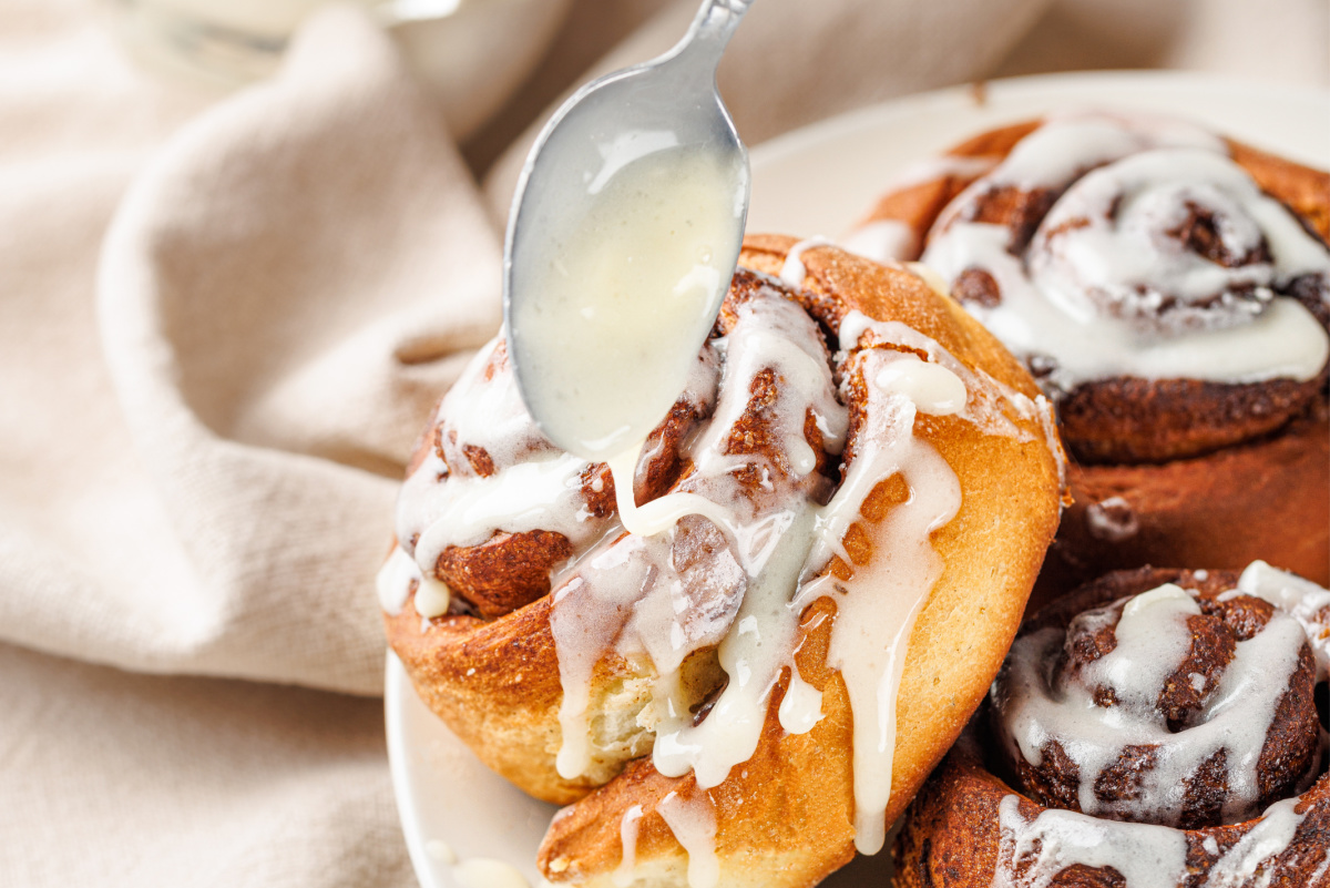 spoon drizzling cream cheese glaze on cinn roll