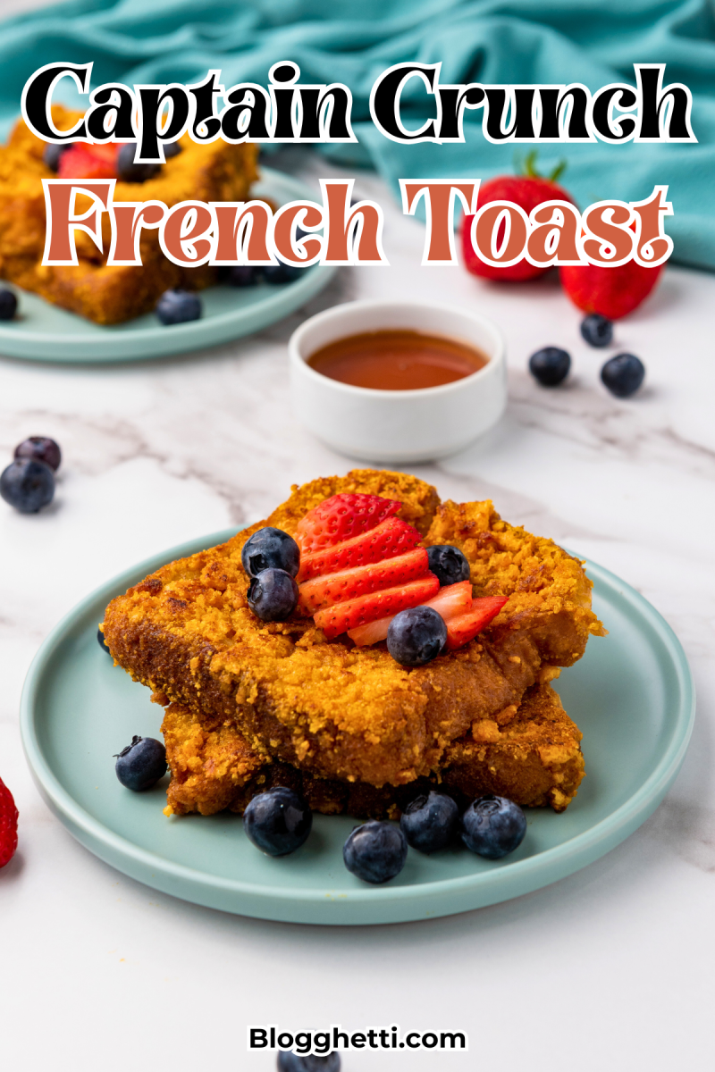 A stack of golden-brown French toast slices coated in crushed Captain Crunch cereal, topped with fresh strawberries and blueberries. A small bowl of syrup is nearby on a white marble surface.