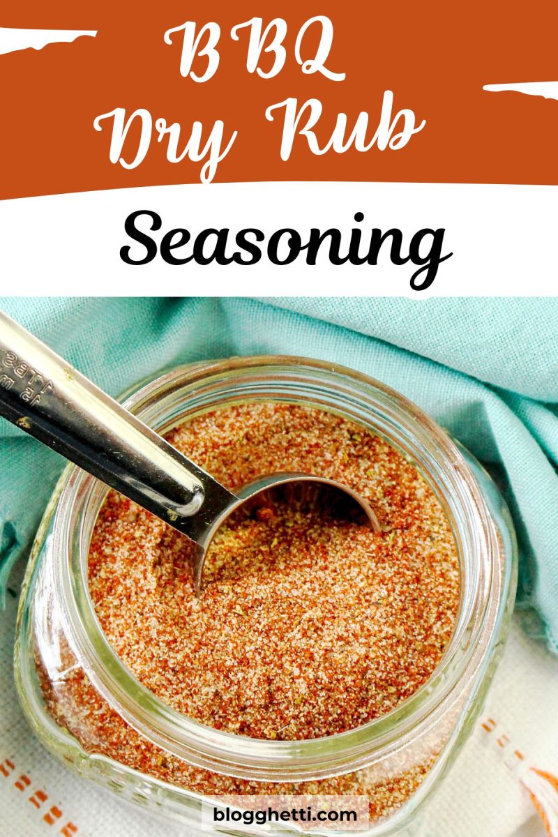 A close-up shot shows a clear glass jar filled with a reddish-brown BBQ dry rub seasoning. A silver measuring spoon rests inside the jar, partially submerged in the spice blend. The jar sits on a light blue cloth with a subtle texture. Above the jar, the text "BBQ Dry Rub Seasoning" is written in a stylized white font against an orange background.