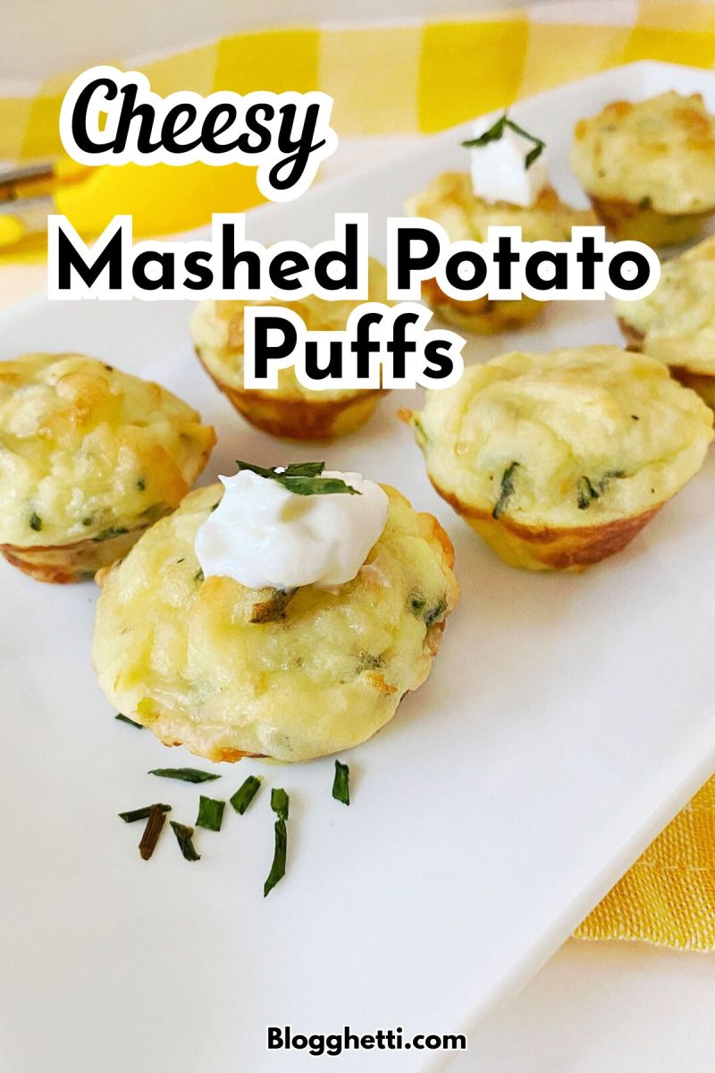 A plate of cheesy mashed potato puffs, garnished with sour cream and chives, sits on a yellow and white checkered tablecloth. The image has the title "Cheesy Mashed Potatoes Puffs" and a website URL "Blogghetti.com" overlaid on it.