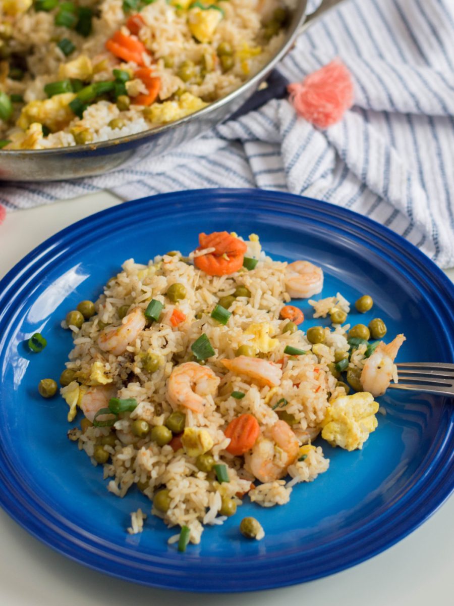 A close-up, slightly elevated view of a serving of shrimp fried rice with visible pieces of shrimp, peas, carrots, and egg on a blue plate.