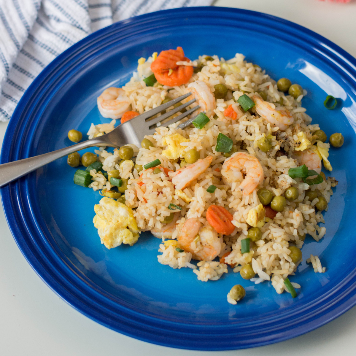 A close-up shot of a fork resting in a serving of shrimp fried rice on a round blue plate.