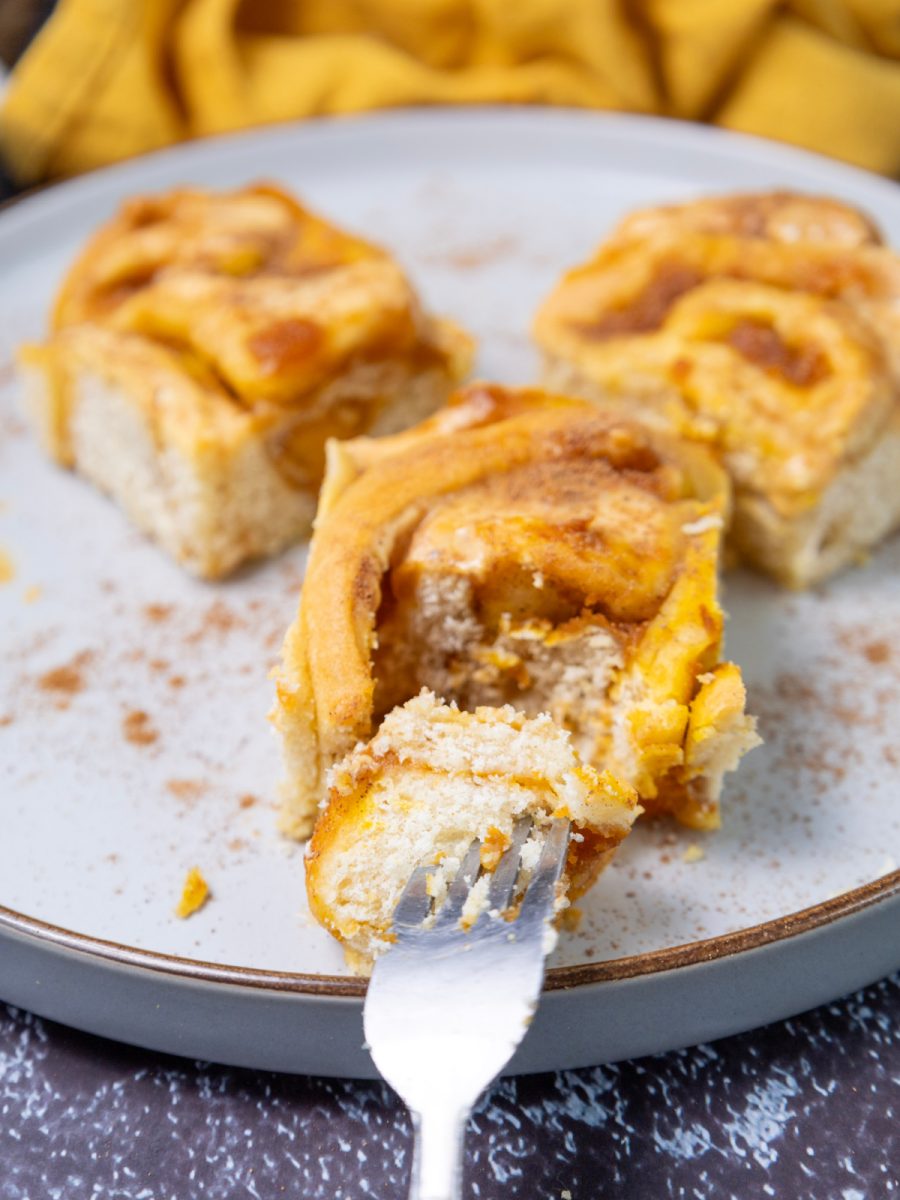 A close-up shot of a fork with a small bite of a pumpkin cinnamon roll on it, showing the soft, moist interior and filling.