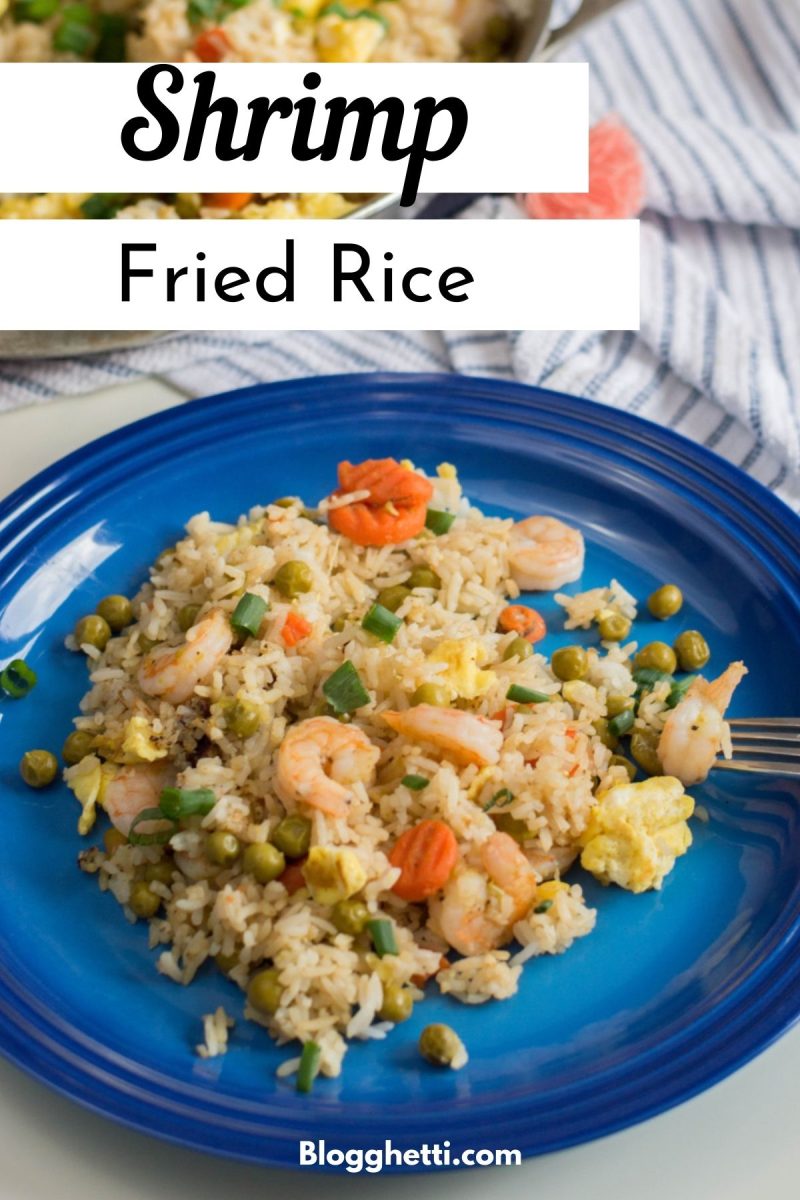 A plate of shrimp fried rice on a blue plate with a serving spoon and a skillet of more rice in the background. The image has the title "Shrimp Fried Rice" and "Blogghetti.com" on it.