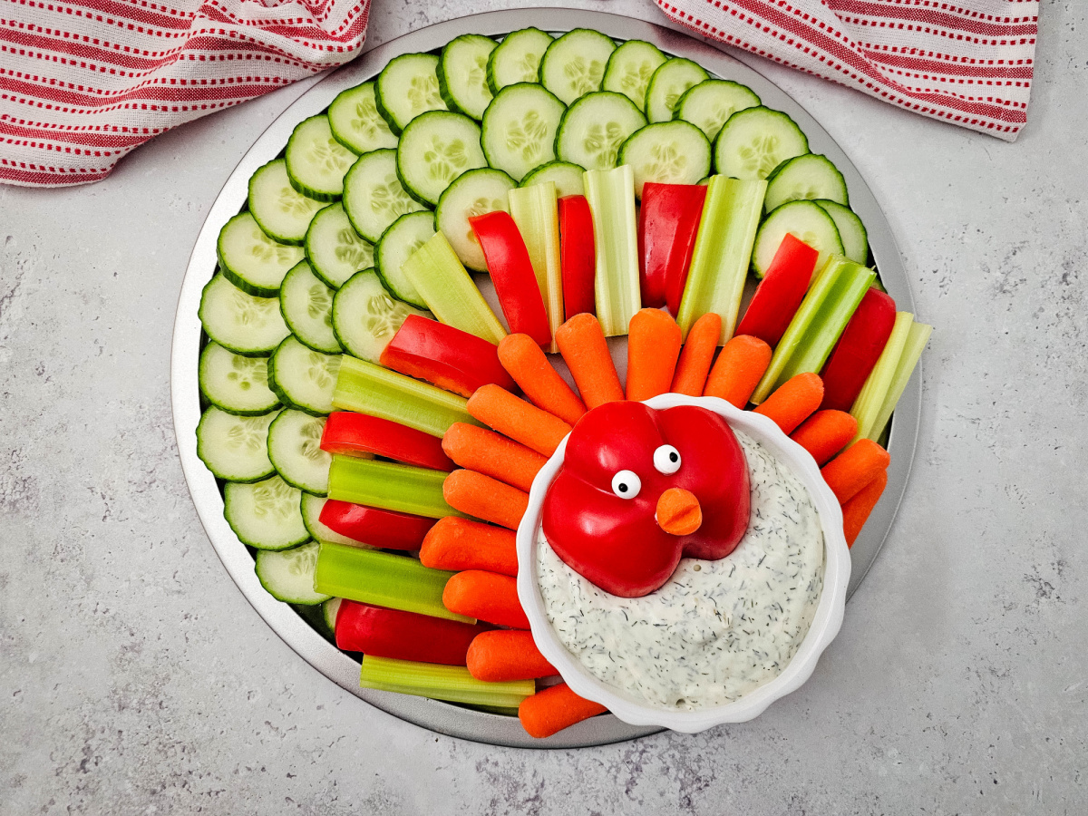A full view of the assembled vegetable tray shaped like a turkey, with a white and red striped towel visible in the background.