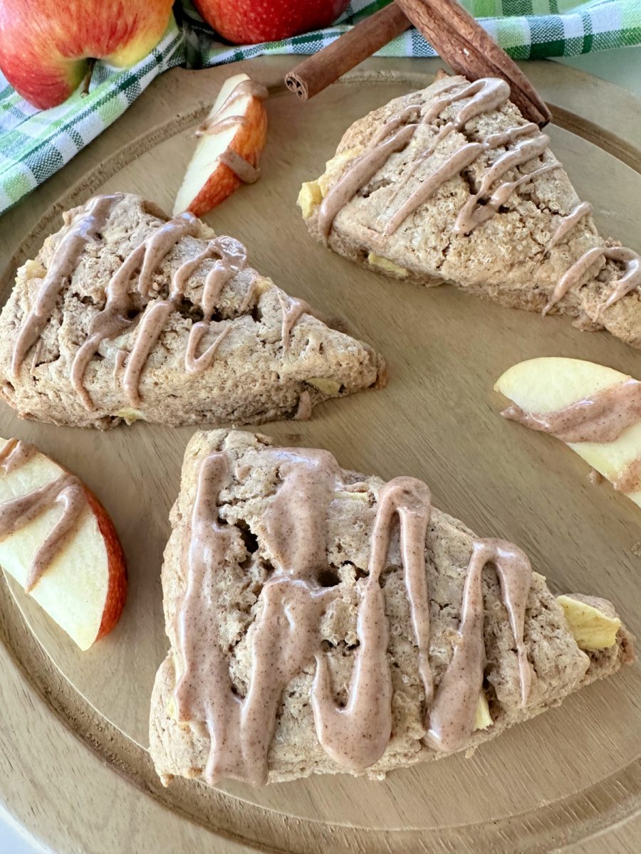 A close-up, eye-level shot of three baked apple chai scones drizzled with glaze, arranged on a wooden board.