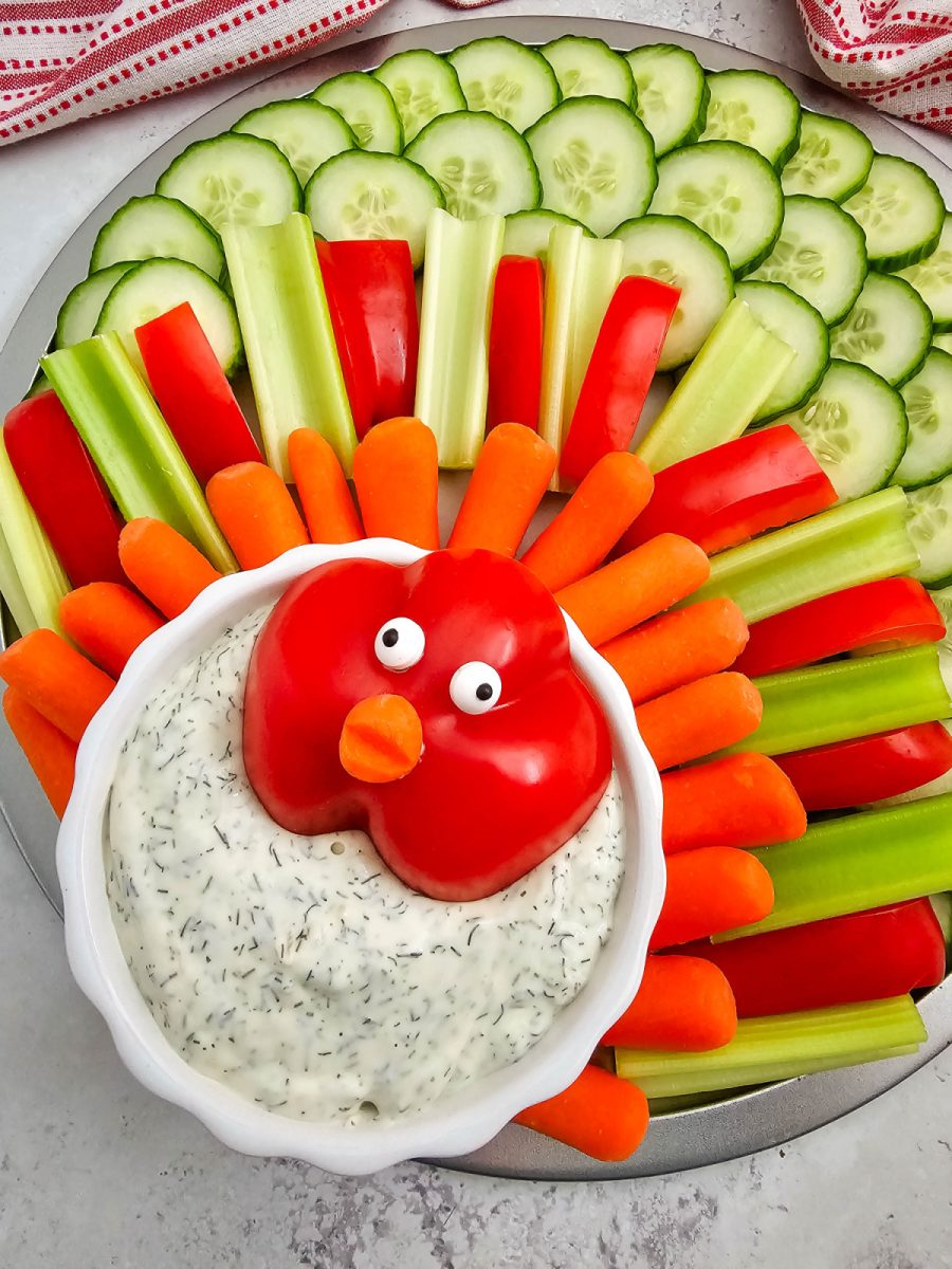 A straight-on, close-up shot of the assembled Thanksgiving turkey veggie platter, showcasing the colorful vegetable "feathers" and the red bell pepper turkey head on the bowl of dip.