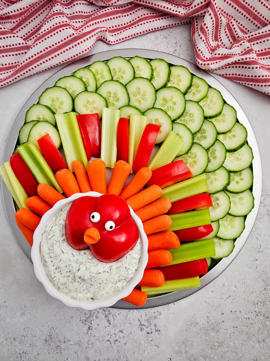 A vegetable tray arranged in the shape of a turkey with cucumber slices as the outer feathers and alternating red pepper, celery, and carrot sticks as the inner layers.