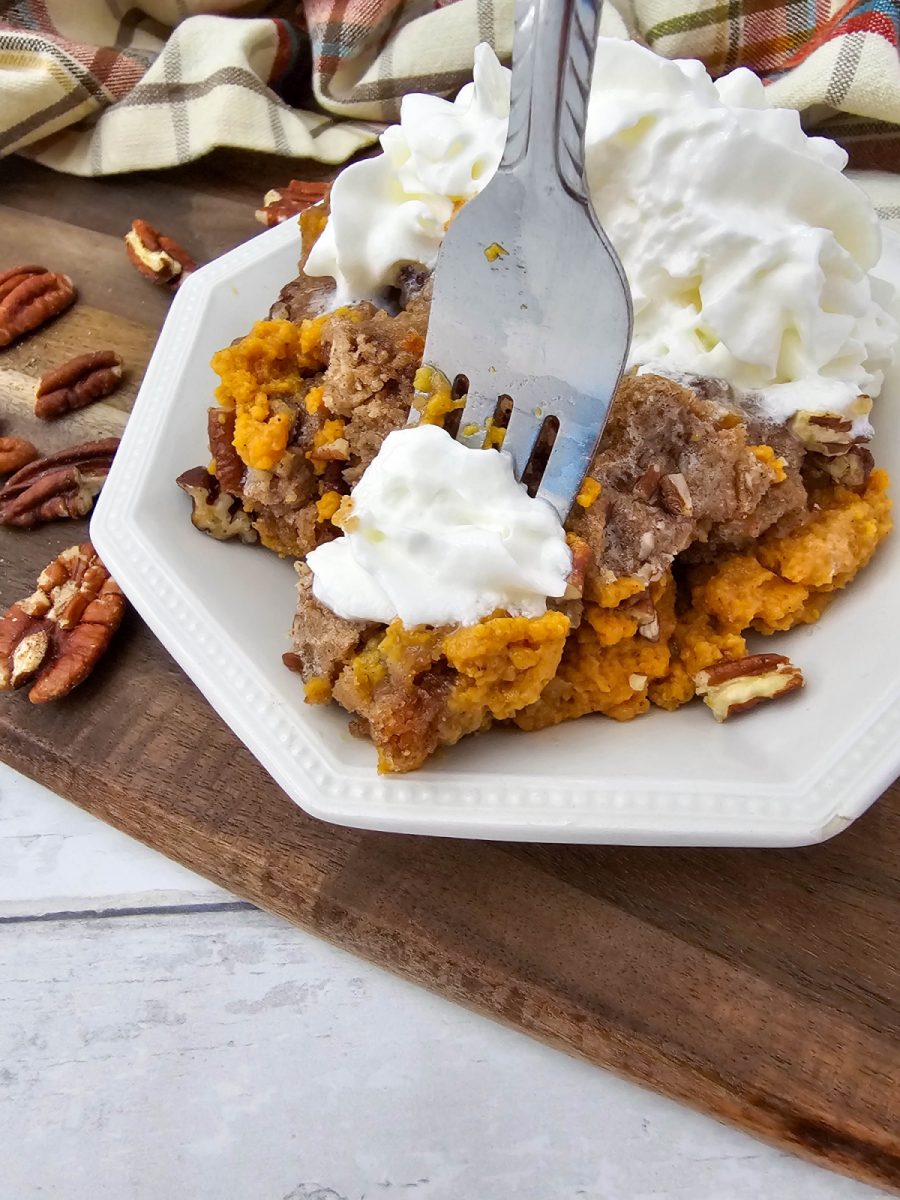 A close-up shot of a fork digging into a serving of pumpkin dump cake topped with whipped cream, highlighting the rich texture of the pumpkin layer and the buttery cake crumble.
