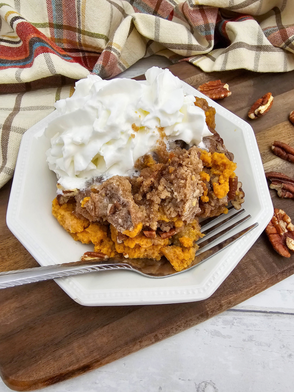 A close-up serving of warm Crock Pot Pumpkin Dump Cake on a white plate, featuring a creamy orange pumpkin custard base topped with a buttery, golden-brown crumble and pecans, finished with a generous dollop of whipped cream.
