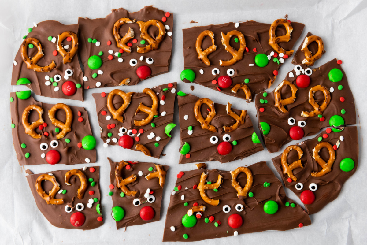 An overhead view of the Reindeer Chocolate Bark on a white surface, broken into individual pieces, clearly showing the 12 completed reindeer faces.
