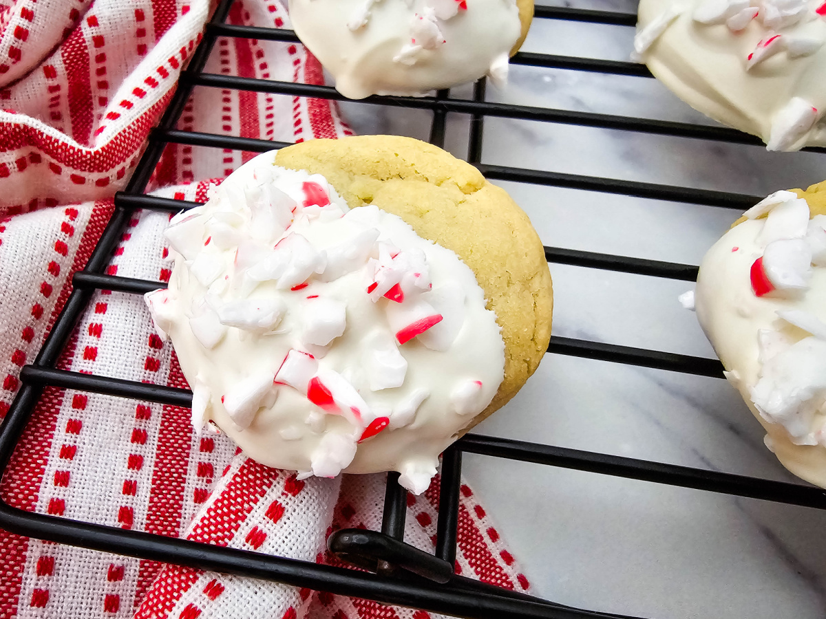 Close-up of a single finished cookie resting on a black wire rack, showcasing the rich white chocolate and crushed peppermint topping detail.