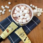 Close up view of homemade hot cocoa flavored with almond and vanilla, served in a white mug and topped with large melting marshmallows. The extract tubes are visible in the foreground.