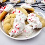 Feature photo showing a pile of peppermint cookies dipped in white chocolate and finished with vibrant crushed candy canes.