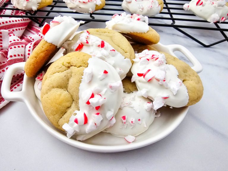 Feature photo showing a pile of peppermint cookies dipped in white chocolate and finished with vibrant crushed candy canes.