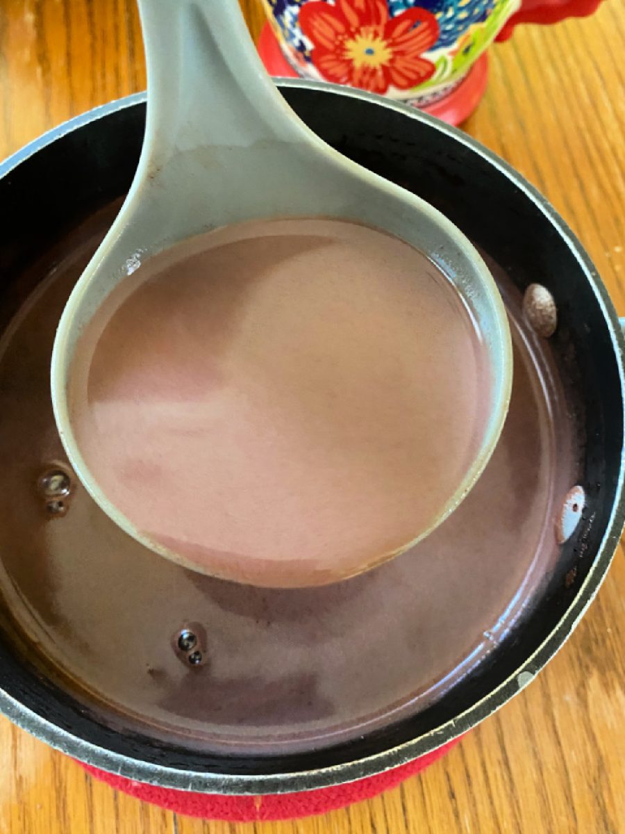 Close-up of a ladle scooping the finished hot chocolate flavored with almond and vanilla from the saucepan, ready to be served.