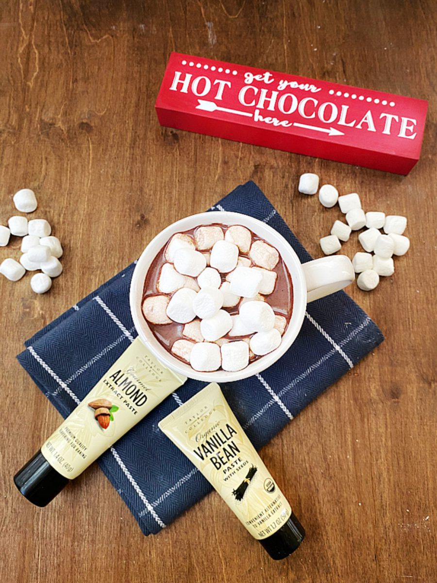 Overhead photo of hot chocolate flavored with almond and vanilla in a white mug, surrounded by the Taylor & Colledge extracts and mini marshmallows.