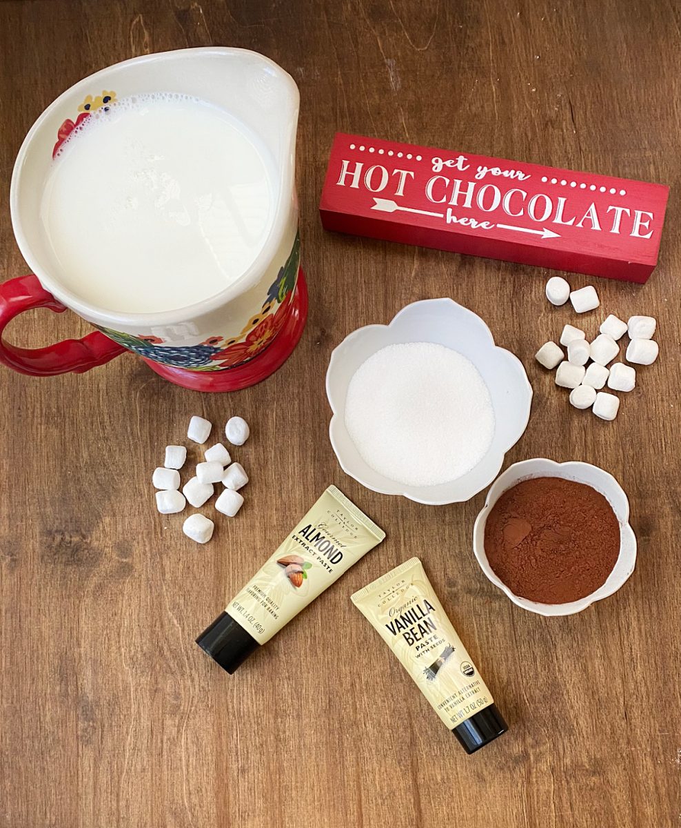 Flat lay photo showing ingredients for Vanilla and Almond Hot Chocolate: milk, cocoa powder, sugar, mini marshmallows, and tubes of Taylor & Colledge Vanilla Bean and Almond extract pastes.