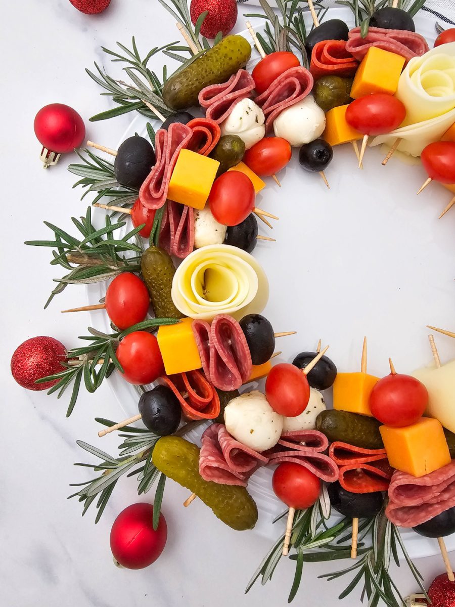 Close-up, vertical shot of the left side of the Simple Christmas Wreath Charcuterie Board, featuring layers of provolone roses, salami, cheddar cubes, tomatoes, and rosemary garnish.