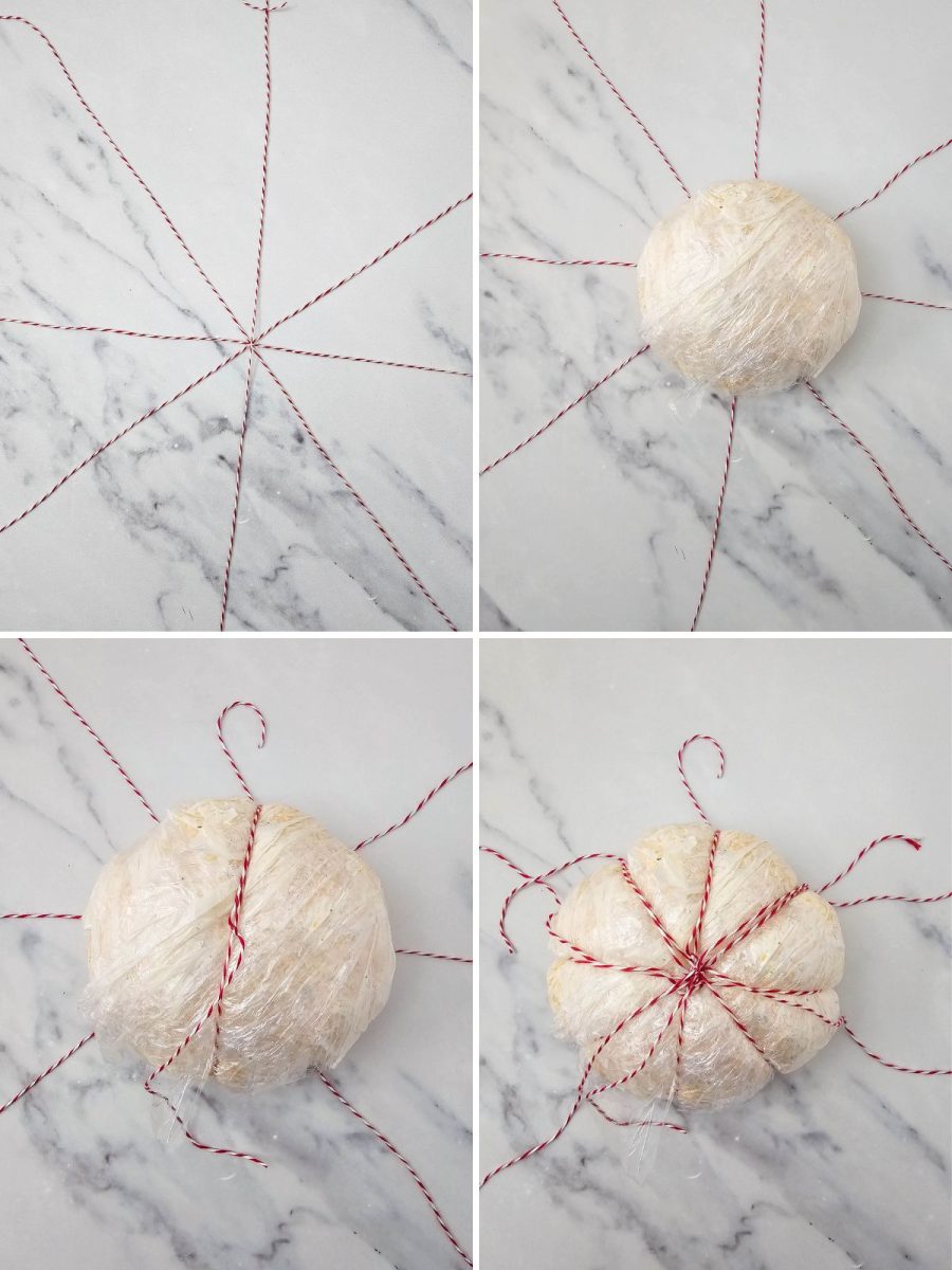 A four-panel collage illustrating how to use baker's twine to create the pumpkin shape for the cheese ball. Top left shows four pieces of red and white baker's twine arranged in a star pattern on a white marble surface. Top right shows the plastic-wrapped cheese ball placed in the center of the twine. Bottom left shows two pieces of twine tied over the top of the cheese ball, creating the first set of grooves. Bottom right shows all four pieces of twine tied, creating a distinct pumpkin shape in the wrapped cheese ball.