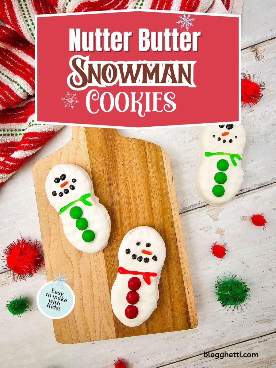Overhead shot of three white-dipped Nutter Butter Snowman cookies decorated with red and green scarves and buttons, arranged on a wooden cutting board surrounded by red and green decorative pom-poms.