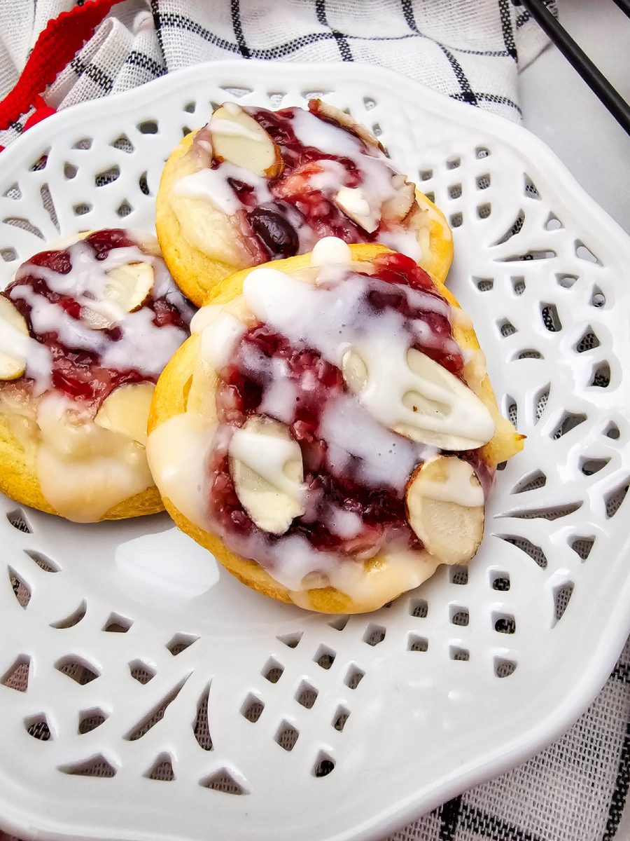 white plate.jpg	Close-up, overhead view of three glazed raspberry cream cheese crescent cookies on a white decorative plate, topped with sliced almonds.