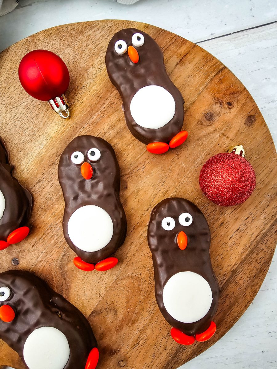Overhead shot of five finished chocolate peanut butter treats with the bird design arranged on a round wooden board with red holiday ornaments.