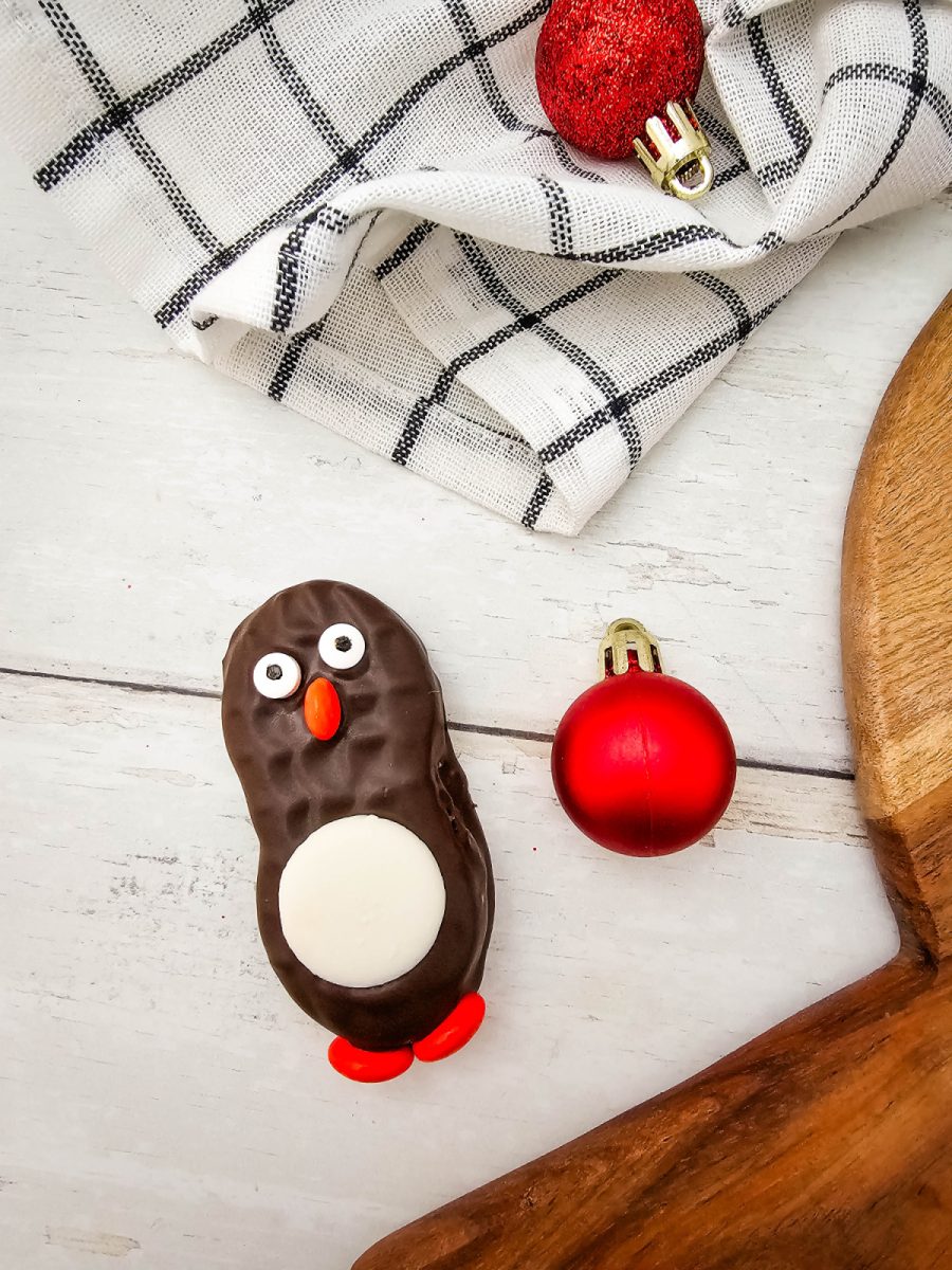 A detailed close-up of a single finished chocolate peanut butter cookie decorated with the bird design, next to a red holiday ornament.