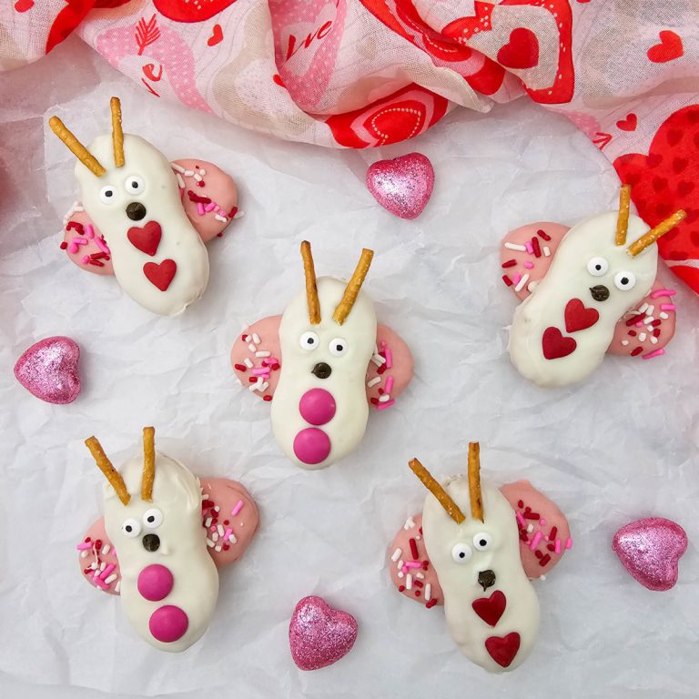 The primary feature image showing a festive spread of six Nutter Butter love bug cookies with pink sprinkles and heart accents on a tissue paper background.,
