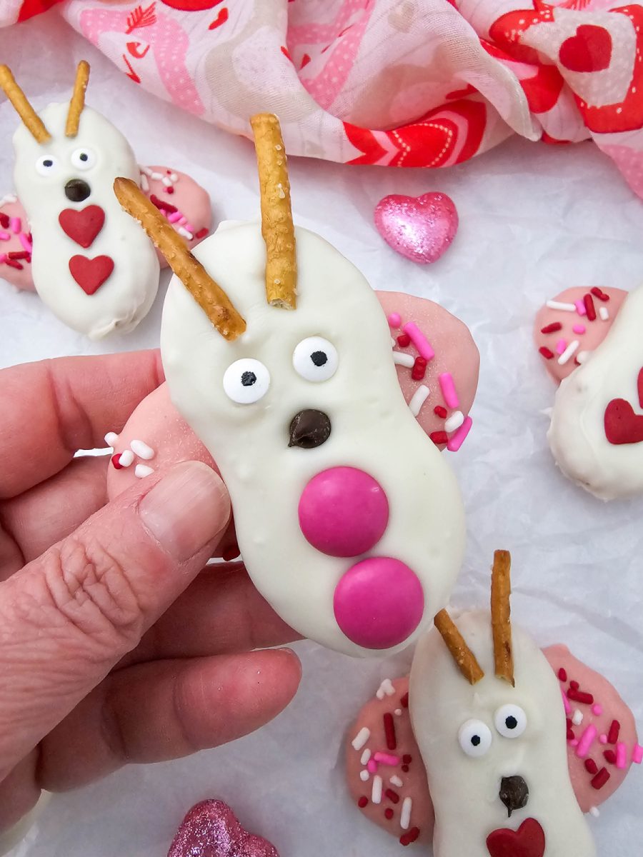 A person's hand holding up a completed Nutter Butter love bug cookie to show its size and decorative candy details.