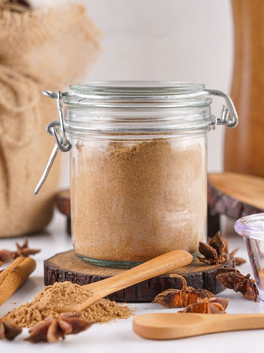 A latch-top glass jar filled with a finely ground brown tea spice blend resting on a dark wood slice.