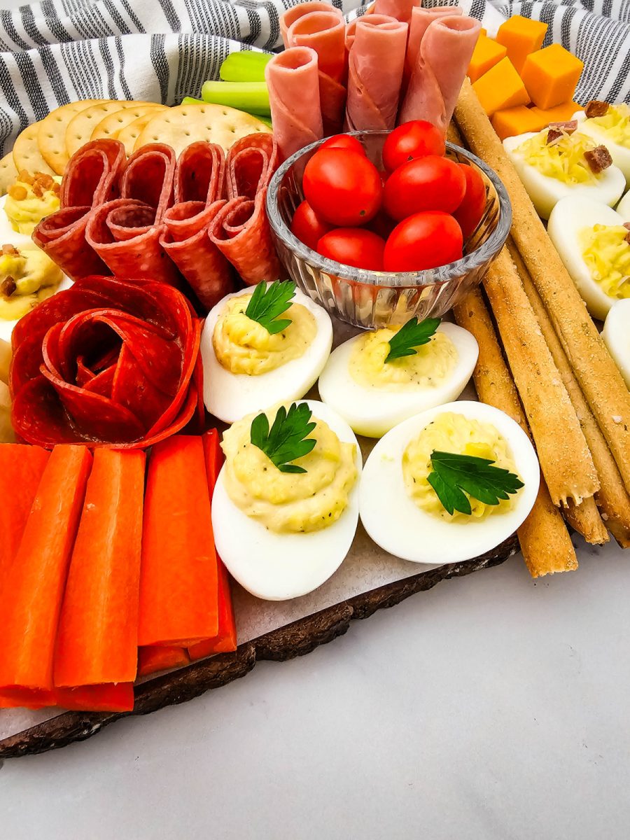 Detailed view of a decorative pepperoni rose placed next to eggs topped with fresh parsley, orange carrot sticks, and long breadsticks.