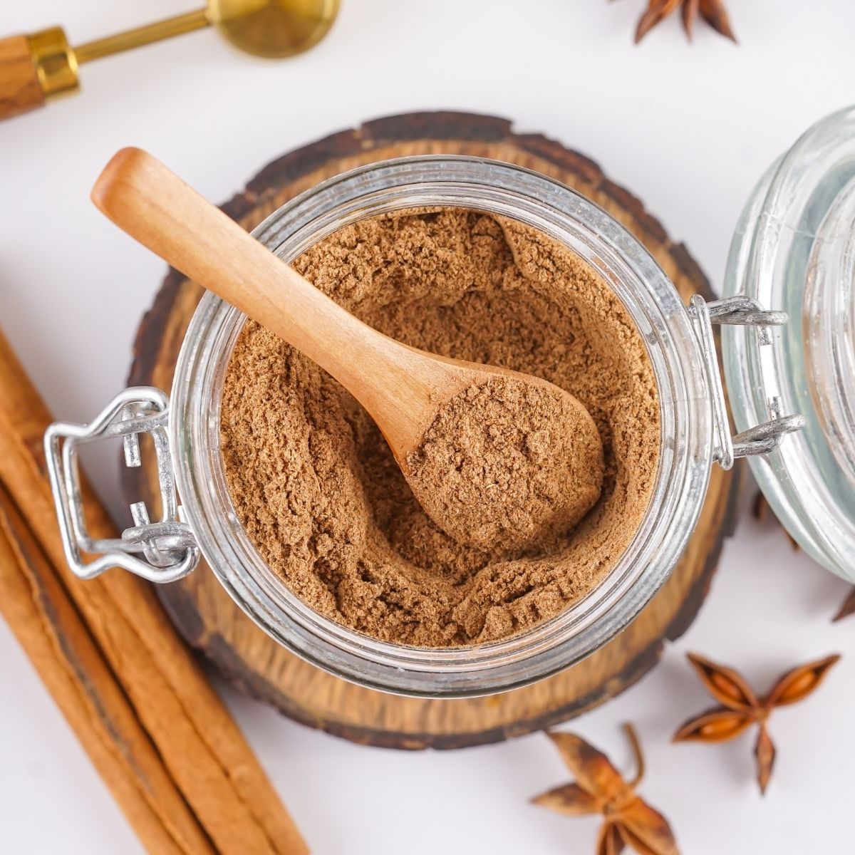 mix.jpg An overhead view of a glass jar containing a powdered chai spice mix with a wooden spoon tucked inside and cinnamon sticks on the side.