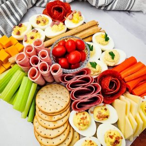 A vibrant and colorful party platter filled with classic stuffed eggs, salami roses, cubed cheddar cheese, celery, and tomatoes.