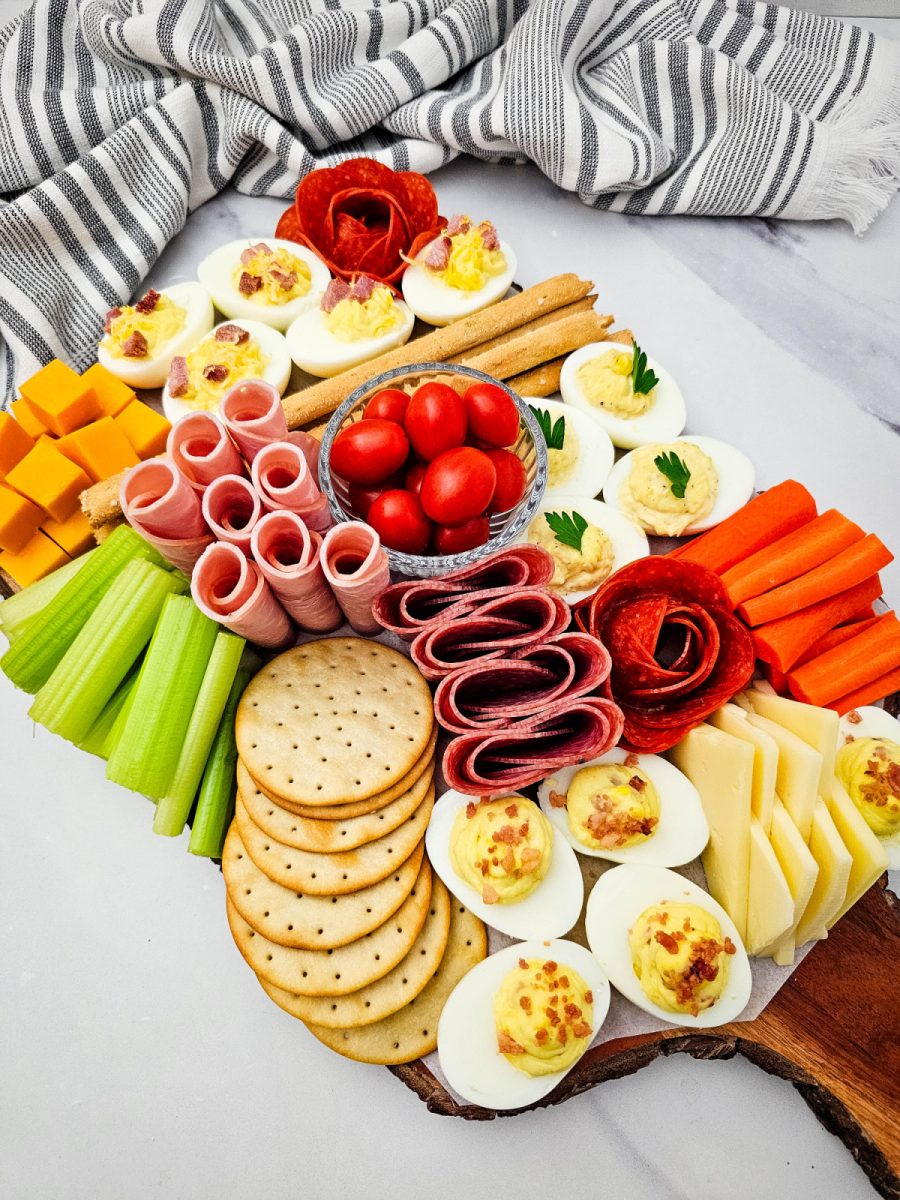 A top-down perspective of a wooden board showcasing a balanced mix of protein-packed eggs, fresh vegetables, and salty crackers.