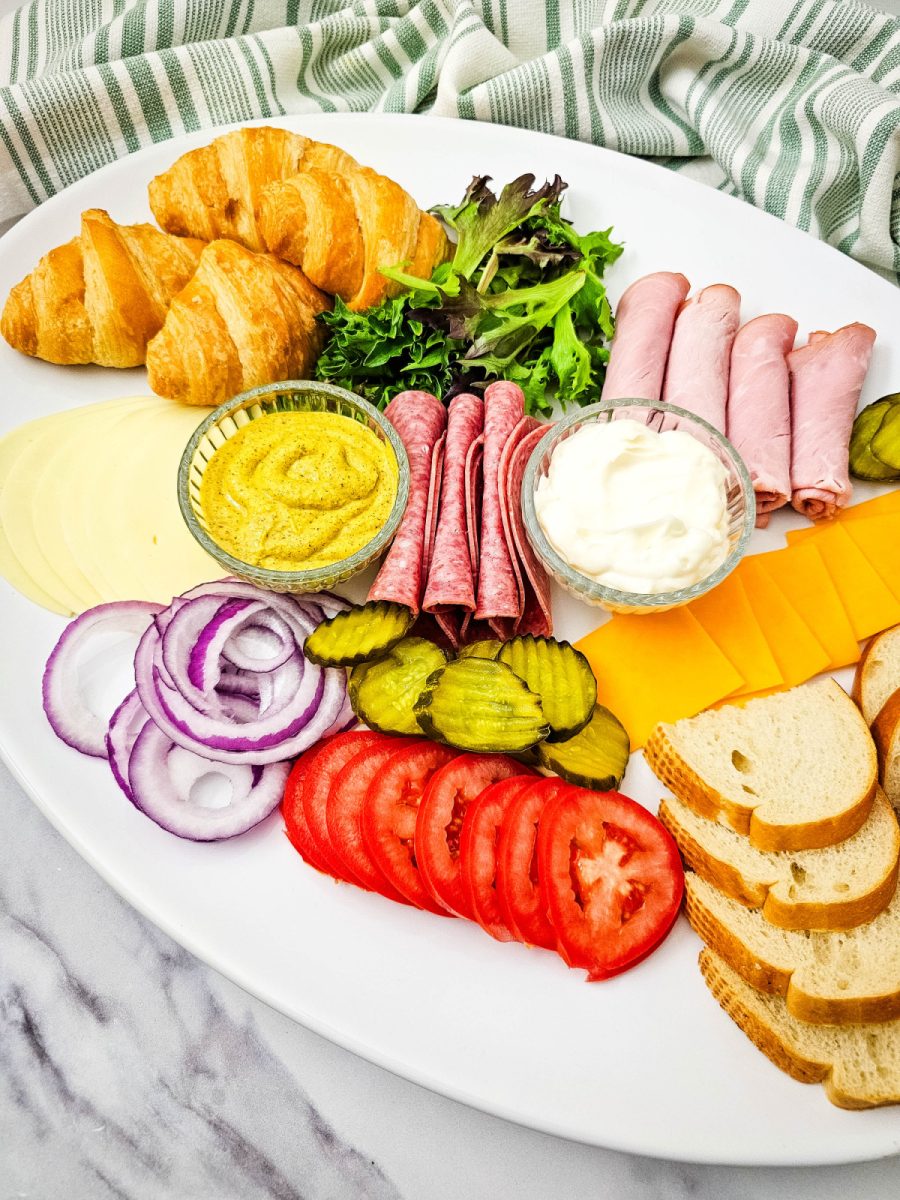 A full view of a large, oval serving tray overflowing with fresh deli fixings. This organized display makes it simple for guests to assemble their own sandwiches using pre-sliced meats, various cheeses, and several condiment options.