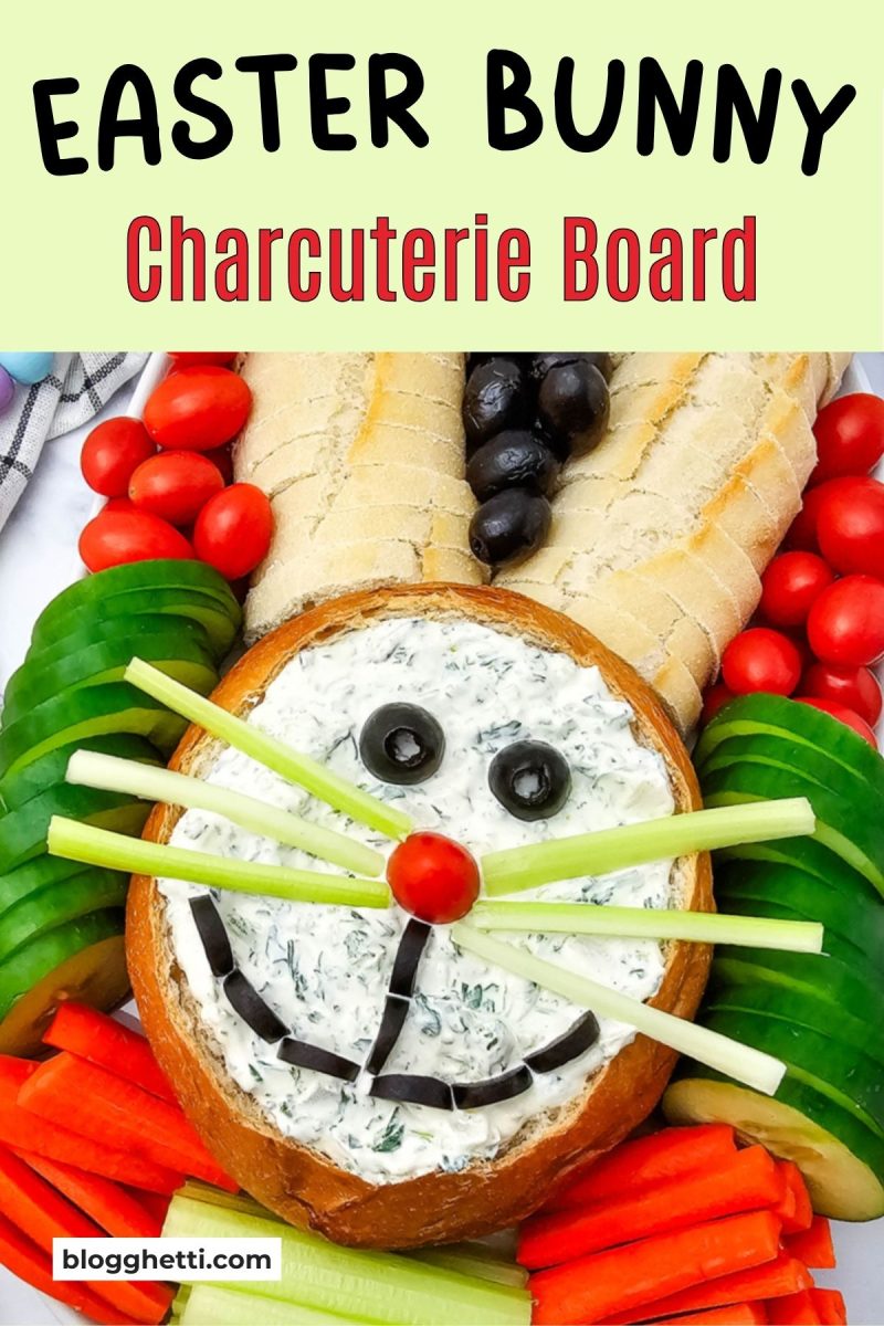 A vibrant spring crudité display featuring a spinach dip centerpiece shaped like a rabbit, surrounded by sliced cucumbers, tomatoes, and baguette rounds.