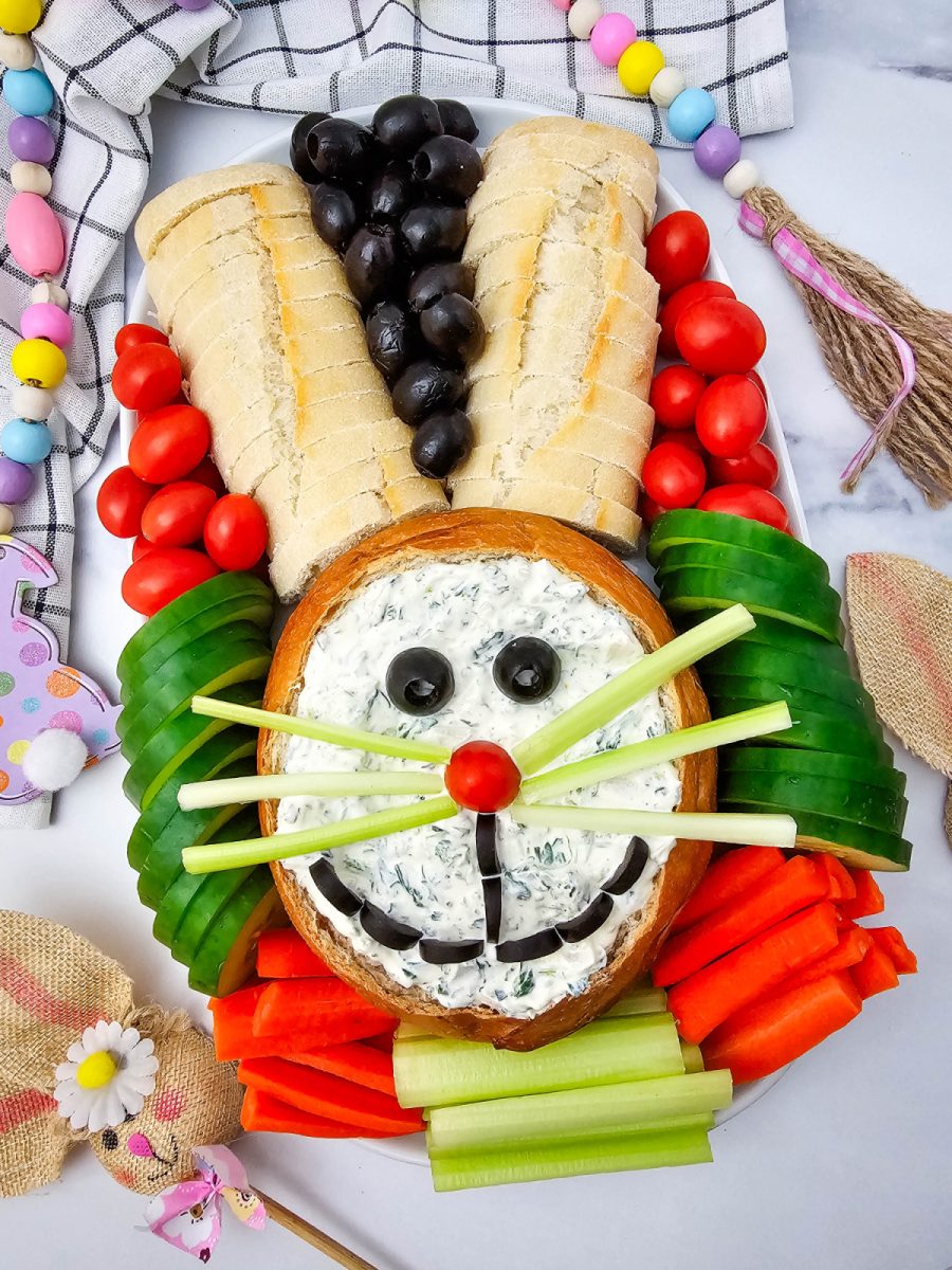 Overhead view of a festive holiday vegetable tray arranged into a rabbit shape with bread slice ears and a variety of colorful fresh produce for dipping.