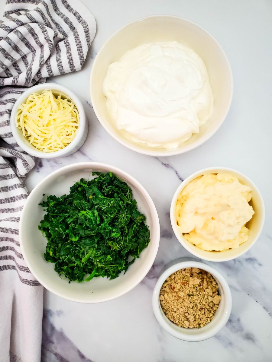 Overhead view of the ingredients for spinach dip including frozen spinach, sour cream, mayo, cheese, and soup mix.