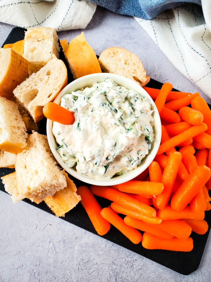 Top down view of a party snack board featuring a bowl of creamy spinach dip with fresh baby carrots and bread.