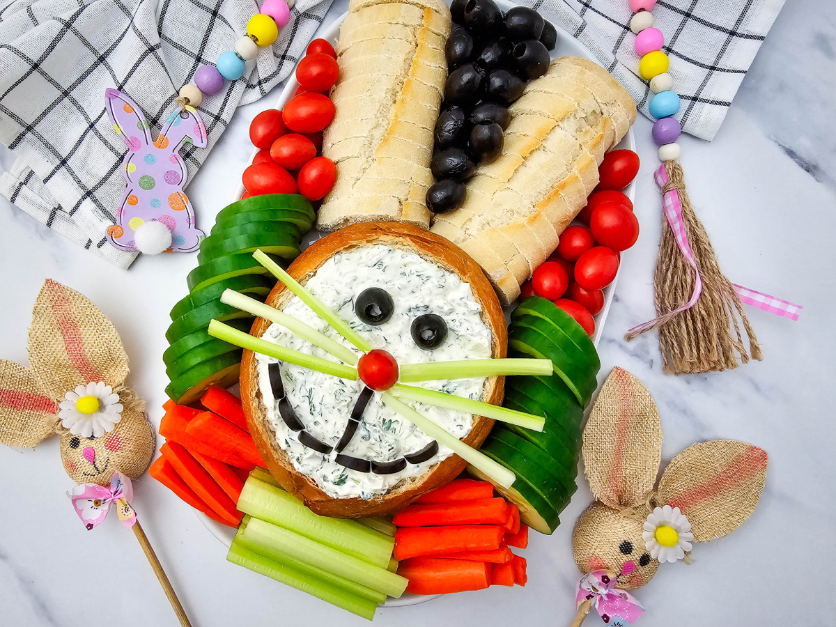 Wide shot of a seasonal party appetizer on a marble surface, featuring a rabbit-shaped dipping station and decorative burlap accents.