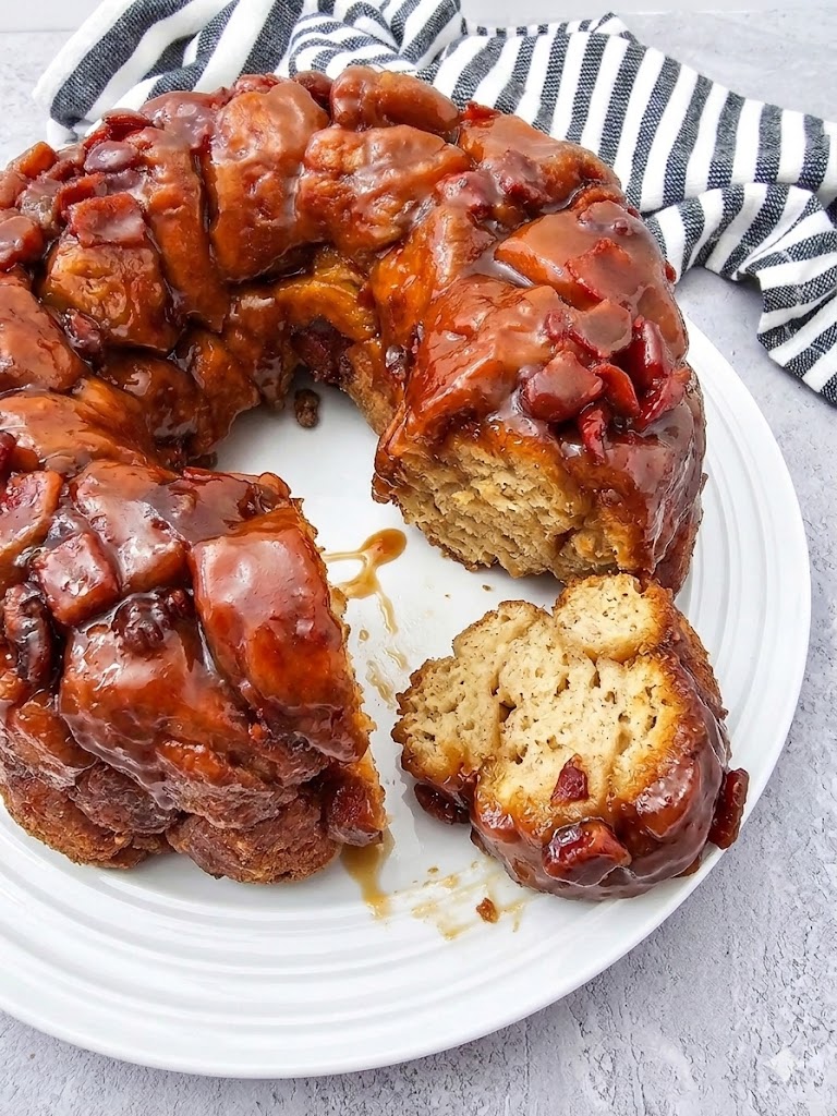 A whole maple bacon monkey bread on a white plate with one sticky piece pulled away to show the fluffy interior.