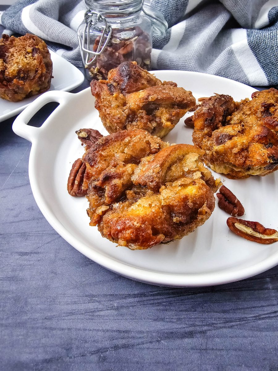 Three golden brown air fryer French toast muffins served on a white handled platter with scattered pecans.